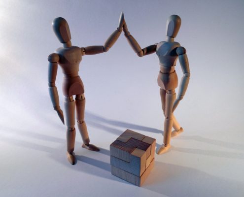 Two artist's mannequins high-five after solving a wooden cube puzzle